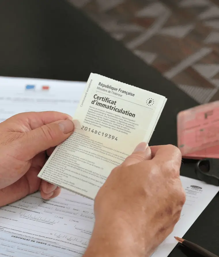 Certificat d'immatriculation français tenu en main, avec le dossier de demande